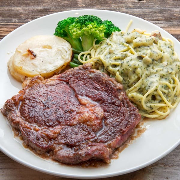 Grilled steak, creamy pasta, roasted potatoes, and broccoli on a white plate at Delicious Food Corner.