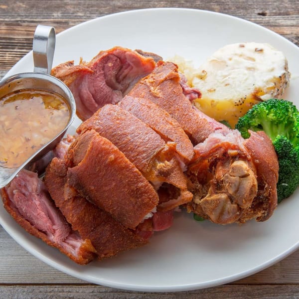 Crispy fried pork hock with gravy, potato, and broccoli on a white plate.
