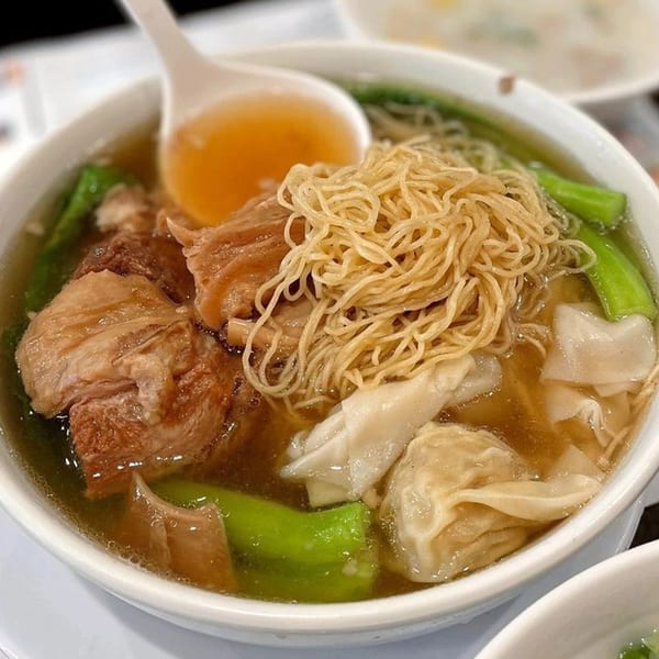 A close-up of Delicious Food Corner's Chinese noodle soup with meat, wontons, and green vegetables.