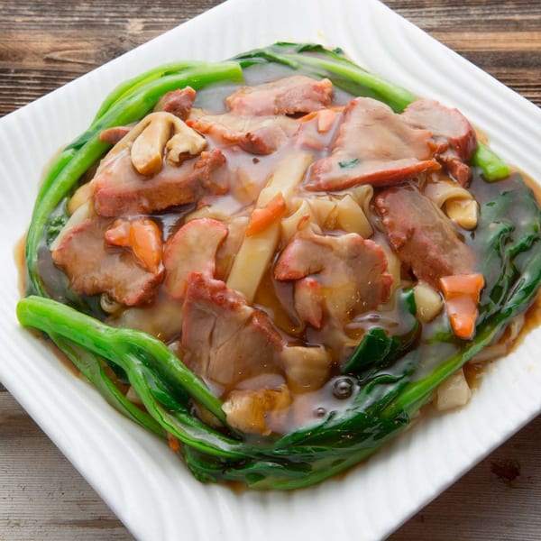 Delicious Food Corner's Chinese dish with sliced meat, noodles, and green vegetables in a rich sauce.