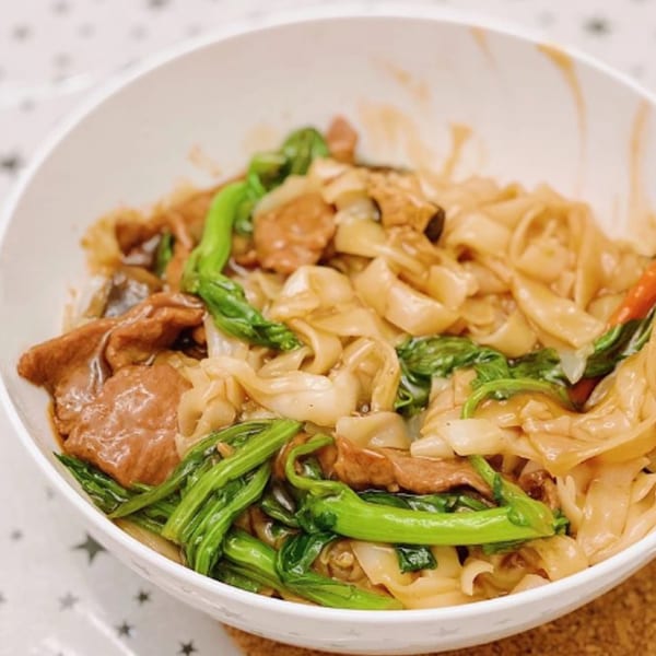 Delicious Food Corner's Chinese beef chow fun with wide noodles and green vegetables in a white bowl.