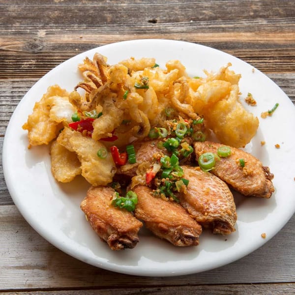 Crispy fried chicken wings and calamari with chopped green onions and red chilies on a white plate.